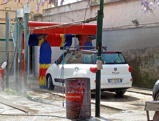 Auto bianca in un autolavaggio automatico con spazzole colorate, servizio di pulizia e manutenzione veicoli