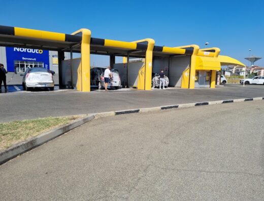 Lavaggio automatico auto presso Norauto: vetture insaponate in fila per la pulizia self-service, box gialli e neri.