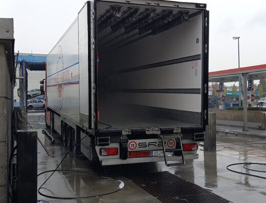 Lavaggio camion presso Autogril Parma: vista posteriore di un camion frigo bianco con portellone aperto, in fase di lavaggio automatico.
