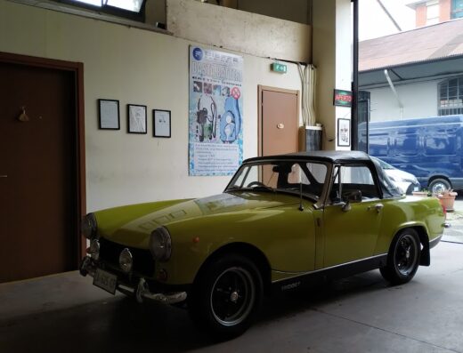 Auto d'epoca gialla Midget in un'officina con insegna 'Aperto', ideale per lavaggio auto CH Service e detailing auto.