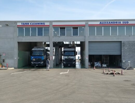 Lavaggio Tank: Vista esterna di un'area di servizio per il lavaggio di cisterne e autocisterne ad Alessandria Sud, con due camion in fase di pulizia.