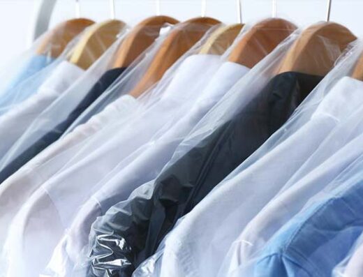 Capi di abbigliamento puliti e stirati appesi a grucce in legno e protetti da buste di plastica, pronti per il ritiro presso la Lavanderia Iodice.