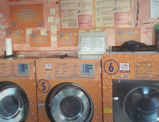 Lavanderia Speedy Wash: primi piani di lavatrici industriali arancioni con oblò in metallo, cartelli con istruzioni in diverse lingue.
