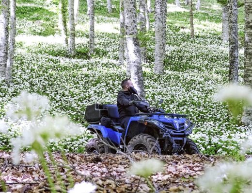 Un uomo guida un quad blu attraverso un bosco fiorito durante un'escursione di Le Cascate Adventure, un'esperienza unica in quad e e-bike.