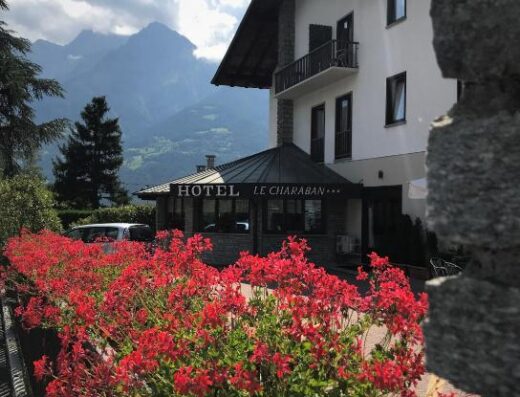 Hotel Le Charaban con fiori rossi in primo piano e montagne sullo sfondo, ideale per viaggi in moto e relax