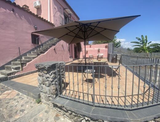 Patio esterno di Le Decime Retreat con ombrellone, tavoli e sedie in ferro battuto, ideale per il relax durante un viaggio in moto