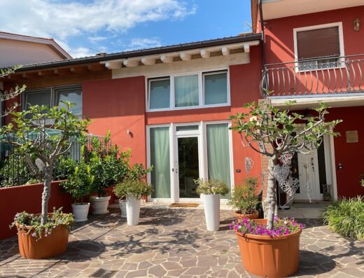 Foto dell'esterno de Le Fate Corbezzole, con piante ornamentali in vaso e facciata rossa, in una giornata di sole.