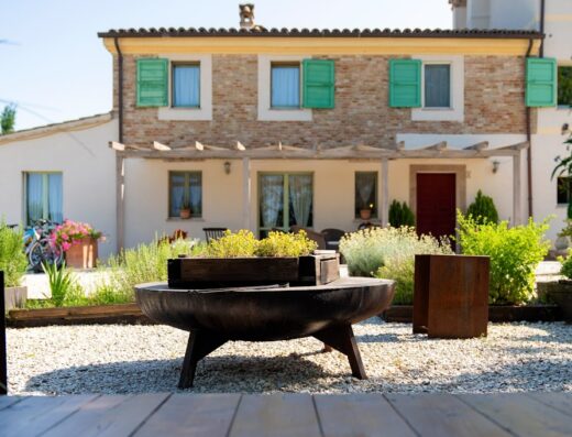 Esterno curato de Le MaRaClà, con braciere decorativo, giardino fiorito e facciata in pietra. Ideale per relax e viaggi in moto.