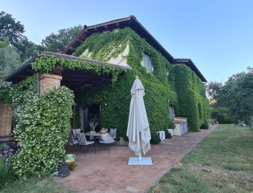 Una pittoresca casa di campagna a Le Mole sul Farfa, ricoperta di edera verde, con un patio accogliente arredato con tavolo, sedie e ombrellone.