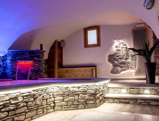 Interno lussuoso de Le Petit Fenestrelle con dettagli in pietra, cascata illuminata, arredamento in legno e illuminazione soffusa, creando un'atmosfera rilassante e di benessere.