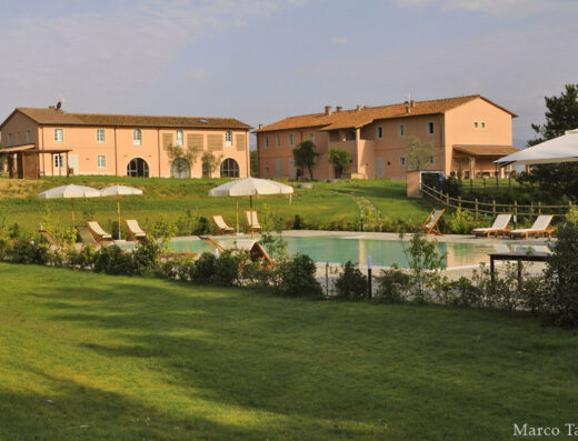 Le Sodole Country Resort & Golf: Vista esterna della piscina con lettini e ombrelloni circondata da prati verdi e edifici in stile toscano.