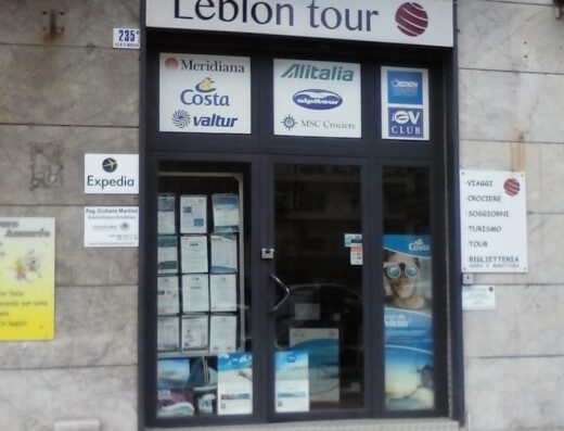 Leblon Tour S.R.L. travel agency storefront featuring logos of airlines like Alitalia and cruise lines like Costa, advertising travel packages, tours, cruises and ticket services.