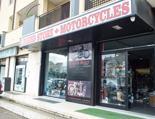 Negozio di motociclette Legend Store con vetrine che espongono caschi, stivali e accessori per motociclisti. Insegna con bandiera canadese e scritta Motorcycles.