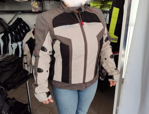 Una persona indossa una giacca da moto Lexel grigia, nera e beige in un negozio di accessori per motociclisti. Abbigliamento protettivo per la guida.