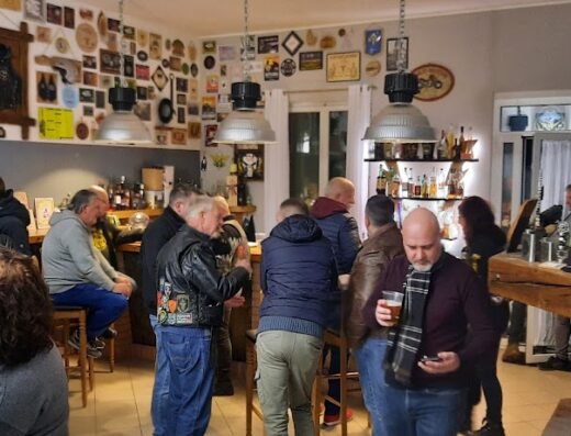 Interno del clubhouse Li Saetis di Cûar, con membri del club di motociclisti riuniti al bar e decorazioni a tema motociclistico.