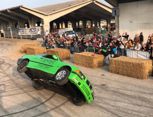 Lo Show dei Motori Fiera Motori: Un'auto verde del Franco Mezici Stunt Team si esibisce in uno spettacolare stunt, guidando su due ruote davanti a una folla entusiasta durante l'evento.