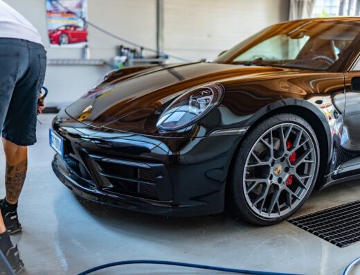 L'Oasi dell'Auto: Dettaglio di una lussuosa Porsche nera durante il lavaggio e la lucidatura professionale, con operatore e attrezzature.