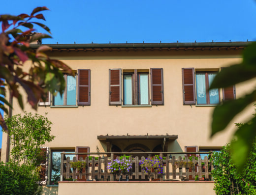 Facciata soleggiata di Locanda Camera con Vista, Toscana, con finestre in legno aperte e balcone fiorito, per un'esperienza di viaggio autentica.