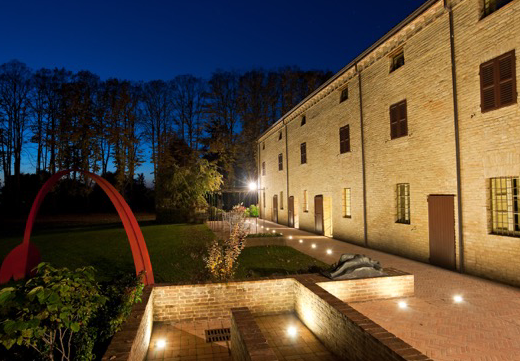 Locanda Del Re Guerriero vista notturna: facciata illuminata, giardino curato con scultura rossa, atmosfera accogliente per motociclisti in viaggio.