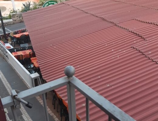 Vista panoramica della Locanda Su Recreu, con tavoli all'aperto coperti da tettoia rossa, ideale per viaggiatori e motociclisti alla ricerca di relax e ristoro.