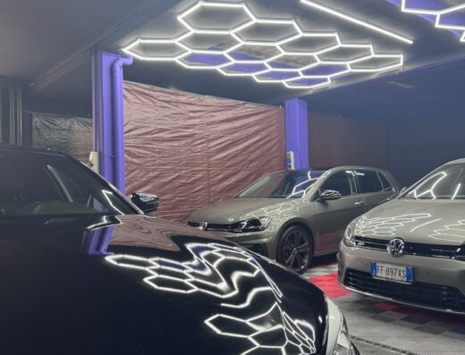 Tre auto parcheggiate in un garage con illuminazione esagonale a LED, tra cui una BMW nera in primo piano e due Volkswagen Golf sullo sfondo.
