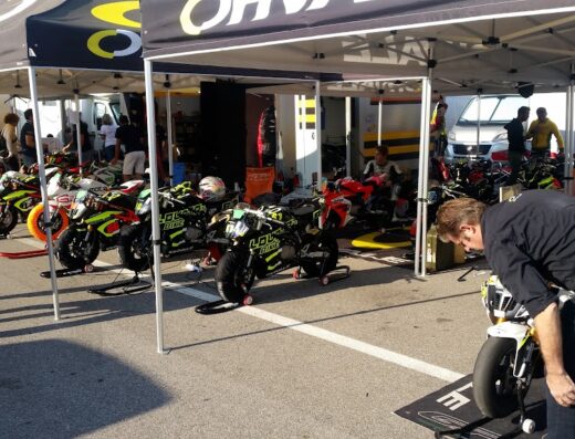 Lovato's Bike motorcycles lined up at a racing event, featuring mechanics and team members under tents, showcasing motorcycle racing and service.