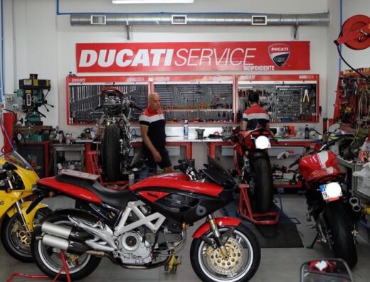 Officina Luciano Moto Roma con moto Ducati in riparazione, meccanici al lavoro e cartello Ducati Service. Vendita, assistenza e accessori moto.