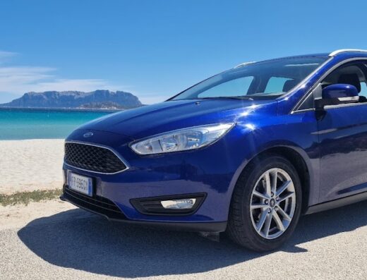 Auto a noleggio LUPOBIKE blu di fronte alla spiaggia di sabbia bianca e mare cristallino, ideale per viaggiare in Sardegna.