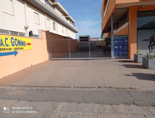 M.A.C. Gomme tire shop entrance in Terralba, Oristano, featuring a yellow sign, metal gate, and service information board. Specializing in tire services for cars, motorcycles, trucks, and agricultural vehicles.