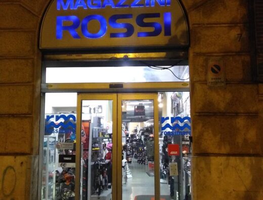 Ingresso del negozio Magazzini Rossi Srl, rivenditore di accessori e abbigliamento per moto e motociclisti, illuminato di sera.