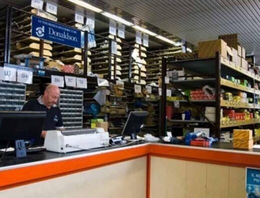 Interno del magazzino dell'auto con scaffali pieni di ricambi e accessori, un addetto alla reception e insegna Donaldson.