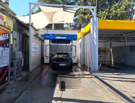 Auto nera in un autolavaggio self-service Makrisè S.r.l.s, con struttura di lavaggio automatica e segnaletica visibile, servizio per la pulizia dei veicoli.