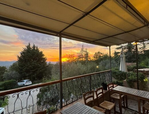 Terrazza panoramica al tramonto dell'Agriturismo Malvarina, con tavoli in legno apparecchiati e vista sulla campagna toscana