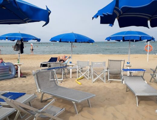 Spiaggia attrezzata presso Manè Boutique Hotel con ombrelloni blu, lettini prendisole e bagnanti sullo sfondo
