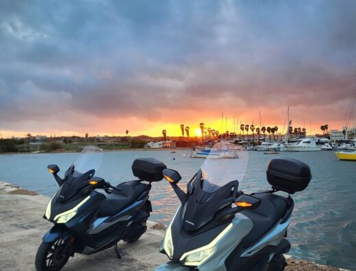 Due scooter Honda Forza parcheggiati sul lungomare al tramonto. Noleggio moto Manganaro per esplorare in libertà.