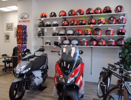 Interno di negozio Mangione Moto: scooter Kymco nuovi, esposizione di caschi moto e accessori per motociclisti.