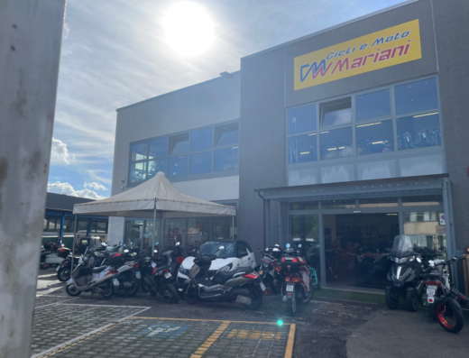 Mariani Cicli e Moto: esposizione di motocicli e scooter davanti al negozio, con un'auto parcheggiata. Servizi di vendita moto e accessori.