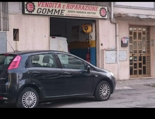 Immagine frontale dell'officina Marino Domenico Gomme, specializzata in vendita e riparazione di pneumatici, con un'auto nera parcheggiata di fronte.