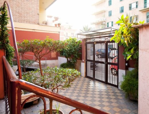 Giardino residenziale con cancello in metallo, vialetto piastrellato a scacchi, lampione e vegetazione rigogliosa, che crea un'atmosfera accogliente e curata.