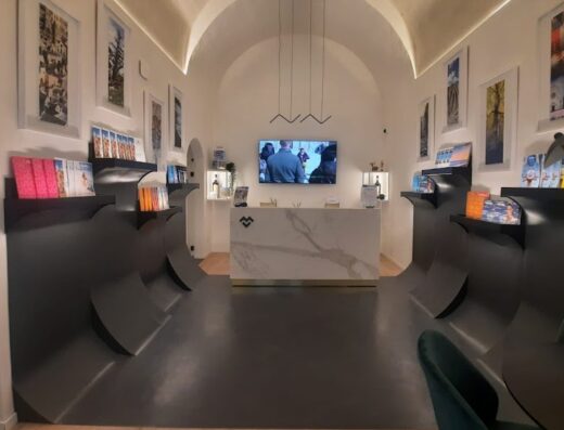 Interni di Martulli Viaggi DMC: design moderno con scaffali curvi, reception in marmo, illuminazione elegante e dettagli di viaggio.