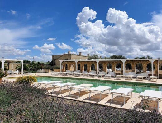 Masseria Agrituristica Lama San Giorgio: Vista della piscina con lettini bianchi, archi in pietra e cielo azzurro con nuvole.