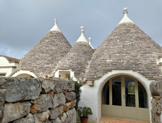 Masseria Camarda features traditional trulli architecture with conical roofs, stone walls, and a rounded doorway in Puglia, Italy.