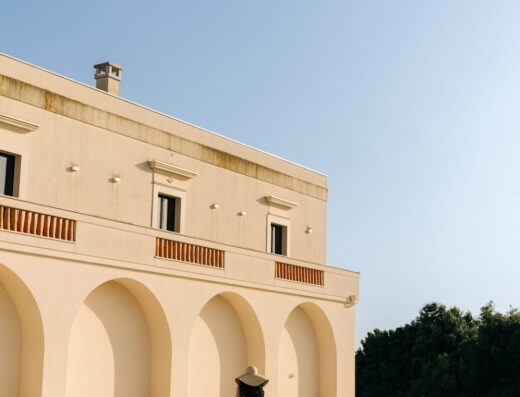 Masseria Fontana Di Vite: A woman in a dress and hat walks away from the camera in the courtyard of the masseria, showcasing the architecture and ambiance of this Italian travel destination.
