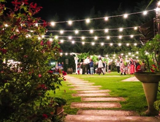 Masseria Montepaolo Dimora di Charme: Un giardino illuminato con luci soffuse, ospita un evento serale con persone in piedi, creando un'atmosfera elegante e accogliente.
