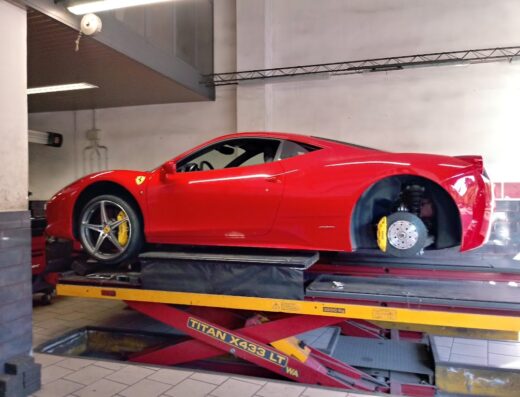 Ferrari rossa su ponte sollevatore in officina per cambio gomme e manutenzione freni. Gomme e accessori auto.