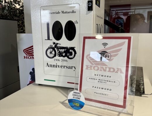 Mattarollo Megastore: Espositore celebrativo del 100° anniversario (1906-2006) con una moto d'epoca, affiancato da un cartello con le credenziali WiFi per la rete Honda. Accessori e servizi per motociclisti.