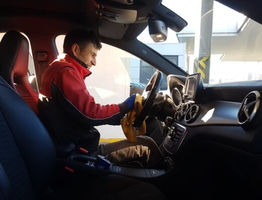 Un uomo pulisce l'interno di un'auto presso Max Autolavaggio di Massimo Silvaroli, concentrandosi sul volante con un panno.