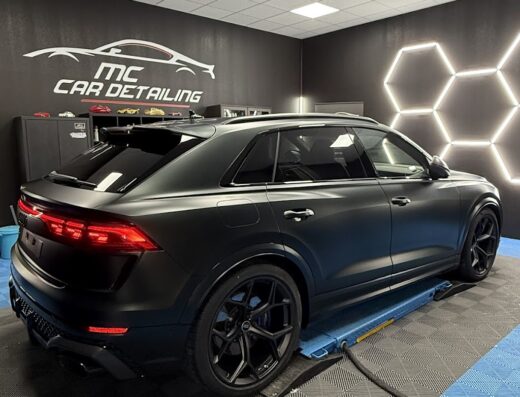 Auto nera opaca su piattaforma elevatrice presso Mc Cardetailing, con logo luminoso e dettagli di design. Servizi professionali per cura auto.