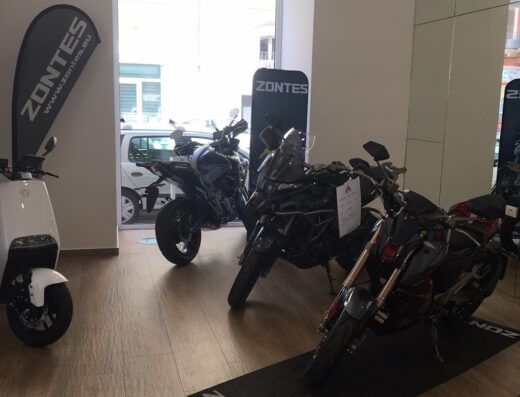 Esposizione di moto Zontes in concessionaria: scooter bianco, adventure bike nera e moto naked rossa in vendita.