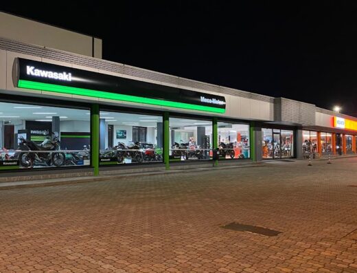 Esterno del negozio Meca Motor con vetrine illuminate che mostrano moto Kawasaki in esposizione. Servizi di vendita e assistenza per motociclisti.